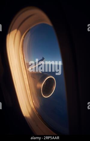 View from airplane window during flight above clouds at dawn. Selective focus on jet engine and aircraft wing. Stock Photo