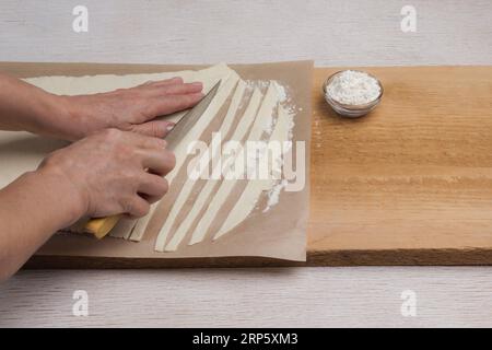 Hand cuts rolled dough into strips with knife. Process of making homemade pasta. Natural food Stock Photo