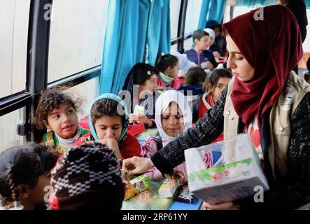 (181230) -- Baghdad, Dec. 30, 2018 -- A teacher hands out juice to displaced children on the Hope Bus in Baghdad, capital of Iraq, on Dec. 27, 2018. At a forgotten slum in the southeast of Baghdad, capital of Iraq, a glimmer of hope shines in the hearts and minds of dozens of internal displaced children as a nongovernmental organization (NGO) turned a large old bus into a mobile school. It is named Hope Bus, the seats of which were removed and replaced with school desks for as many as 50 pupils, and was furnished with colorful curtains, loudspeakers, a television set and a blackboard. The chil Stock Photo