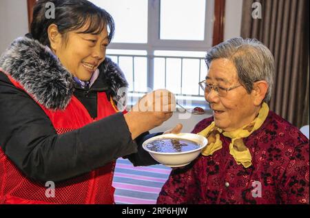 (190114) -- BEIJING, Jan. 14, 2019 -- A volunteer feeds Laba porridge to an elderly woman at a nursing home in Anping, north China s Hebei Province, on the Laba Festival on Jan. 13, 2019. The Laba porridge is made from a dozen varieties of grains including glutinous rice, millet, Chinese sorghum, peas, dried lotus seeds, and red beans. Laba falls on the eighth day of the 12th lunar month. The Laba Festival is considered a prelude to the Spring Festival, or Chinese Lunar New Year, which falls on Feb. 5 this year. Chinese people believe the festival meal of Laba congee bears the auspicious meani Stock Photo