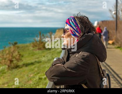 portrait of a woman in a jacket standing on the embankment and looking at the sea Stock Photo
