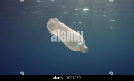 Disposable plastic bottle drift under surface of water in sunrays. A plastic bottle is thrown into the sea slowly drifts in water column in rays of Stock Photo