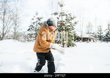 Little cute boy in black hat,orange jacket is lying,playing in snow. Kid walking in beautiful frozen forest,park among fir snowy trees. Winter vacatio Stock Photo