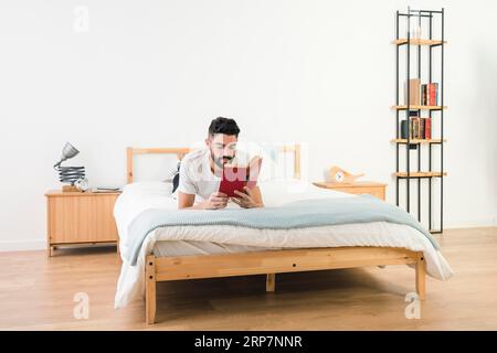 Man lying bed reading book bedroom Stock Photo