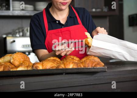 Close up female baker putting croissant paper bag Stock Photo