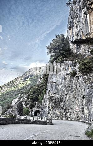 Photo with reduced dynamic range saturation HDR of view of steep rock face next to mountain road in French Maritime Alps, veil clouds above Stock Photo