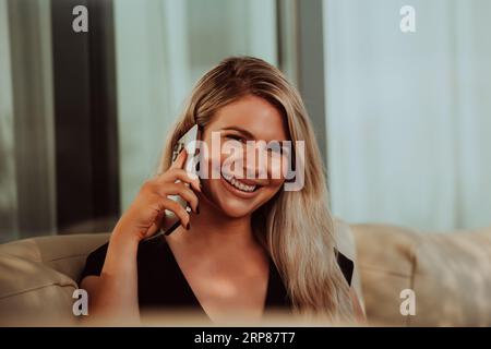 A modern and confident businesswoman, with a cheerful smile, engages in a successful phone conversation, indicating the accomplishment of a new Stock Photo