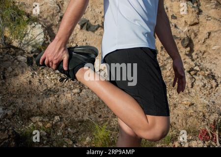 Close-up of a young Caucasian sportsman doing stretching in a park. He is flexing his right leg Stock Photo