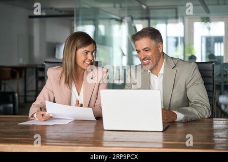Two executive managers working on laptop discussing documents at office meeting. Stock Photo