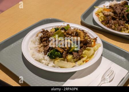 Teriyaki beef and stir-fried vegetables with rice. The dish is at a table in the food court. Stock Photo