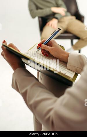 Close-up of a notebook with a pen in the hands of a psychologist taking notes during a psychotherapy session with a man. Psychology, psychotherapy. ve Stock Photo