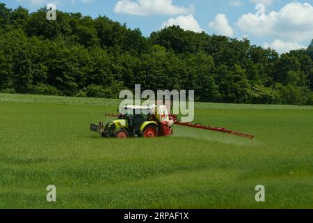 A farmer sprays fertilizer through a sprayer while riding in a tractor in the field. Stock Photo