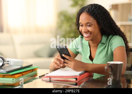 Happy black student checking phone studying at home Stock Photo