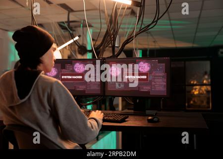 System hacked by cybercriminal reading warning alert, it specialist solving cyberattack problem at night. Working on computer security technology and data breach. Hacker accessing database server. Stock Photo