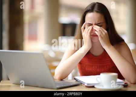 Front view portrait of a student suffering eyestrain after using laptop in a bar terrace Stock Photo