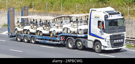 Volvo hgv tractor unit truck and dutch built Nooteboom low loader semi trailer load of Ezgo golf buggies driving along M25 motorway road England UK Stock Photo