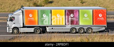 Ocado side view hgv power unit lorry truck driver & multi colour delivery articulated trailer graphics driving along on m25 motorway road England UK Stock Photo