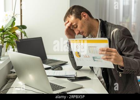 Frustrated overworked caucasian businessman, entrepreneur, product manager, programmer, sits at a desk in the office, massaging the bridge of his nose Stock Photo