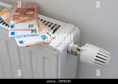 Euro money banknotes on heating radiator battery with thermostat temperature regulator. Concept of expensive heating costs and rising energy bill Stock Photo