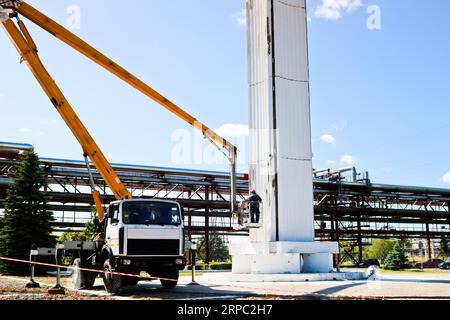 Repair columns on a special technique. Workers on the crane repair a large white column. Cosmetic repair with painting. Workers in a special form pain Stock Photo
