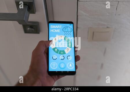 Smartphone with home security app in a hand on the building background Stock Photo