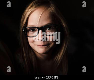Portrait of little girl wearing glasses in low light Stock Photo