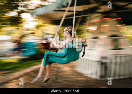 Girl rides chair swings at amusement park on a warm day Stock Photo