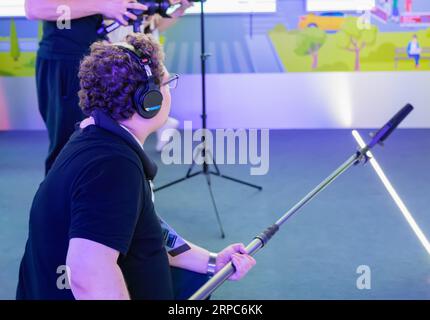 A sound engineer in headphones holds a microphone on an extended boom. Moscow Russia August 19, 2023 Stock Photo
