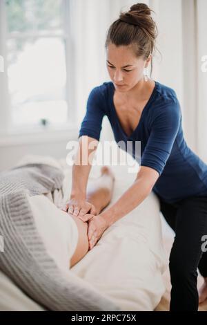 A female massage therapist concentrates on her patient's thigh muscle Stock Photo