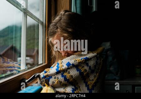 girl in a cosy norwegian jumper looking out the window of a cabin Stock Photo