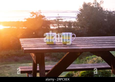 Two plastic coffee mugs on a picnic table in a campsite at sunrise Stock Photo