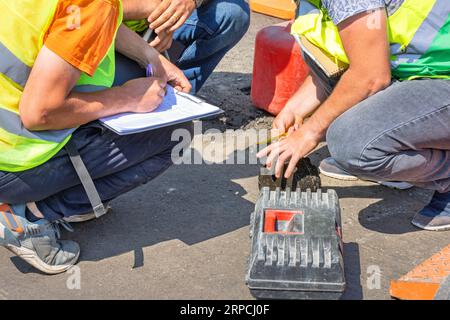 Road maintenance engineers measure the core of the asphalt pavement with a tape measure and record the data in a table. Stock Photo