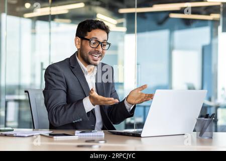 Young successful hispanic businessman talking on video call using laptop, man inside office at workplace, online meeting with colleagues and partners. Stock Photo