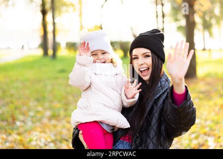 Mother and young little girl with blonde hair are playing in an autumn park on a yellow and orange leaf background. Family is walking in park Stock Photo