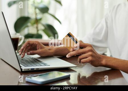 Hands of young male customer with credit card sitting in front of laptop and entering banking data on website page while making online order Stock Photo