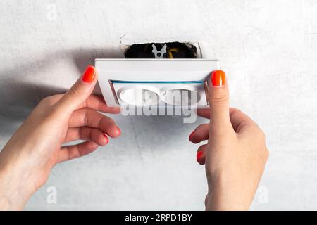 The girl is trying to insert a torn out socket from the socket due to the wrong pulling out of the electrical plug. Stock Photo