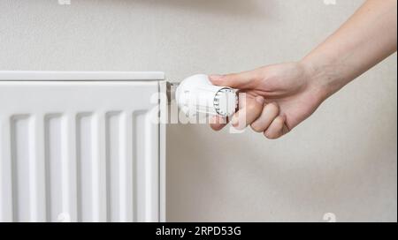 A woman regulates the gas heating in the room in order to save gas energy, taking into account the sanctions. Comfortable heating in the house. Stock Photo