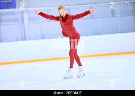 Talented girl, teenager in red sportswear, figure skating athlete in motion, training on ice rink arena Stock Photo