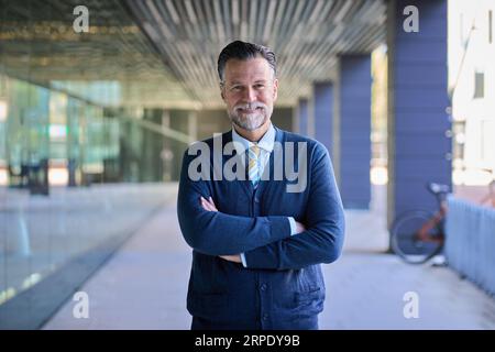 Portrait adult Caucasian gray haired business man happy expression and crossed arms. Finance male. Stock Photo