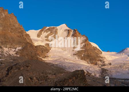 Gran Paradiso mountain and glacier view from chabod hut at sunset. golden hour, colored peak against blue sky. landscape Stock Photo