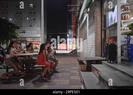 (190818) -- BEIJING, Aug. 18, 2019 -- Children watch television outside a convenience store near a clothes factory in Shishi, southeast China s Fujian Province, Aug. 5, 2019. The scorching heat has been engulfing Shishi of southeast China s Fujian this summer, leaving few walking on the usually-bustling streets. By contrast, clothes factories, which are densely dotted in the city, are crowded with people who have been swamped with their work as summer is the peak season for garment making every year, and also their children. The reputed status of Shishi as a major clothes manufacturer across t