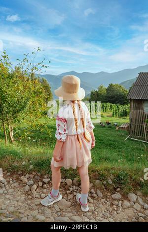 Ukrainian child with long braided hair in authentic costume on farm in Carpathian Mountains village Cute girl embroidered shirt scenic view. Independe Stock Photo