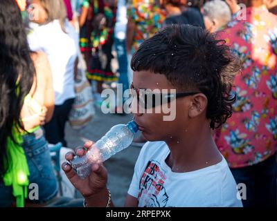 Barranquilla, Atlantico, Colombia - February 18 2023: Dark-haired Colombian Boy Wears Black Glasses while Walking with empty Plastic Bottle Stock Photo