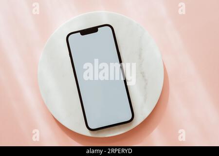 White blank path screen mobile phone with mockup copy space on white marble podium on pink background with shadows. Minimal aesthetic business brand t Stock Photo