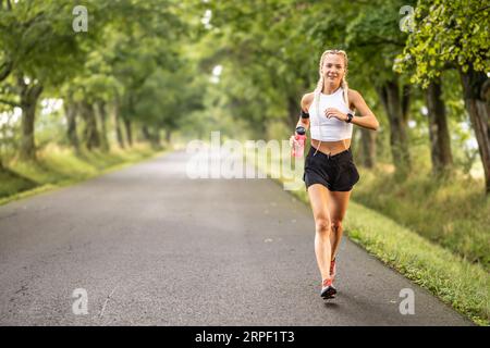 Female runner jogging outside in the park. Young woman runner running with a bottle of water. Stock Photo