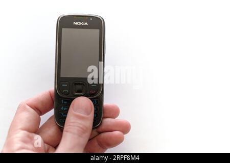 Old well-used dumb cell phone Nokia 6303 ci in a hand. Low-tech mobile concept. Outdated vintage technology working for a long time. Stock Photo