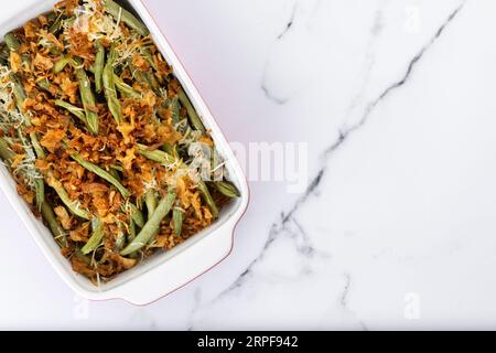 A traditional green bean casserole topped with French Fried Onions and cream of mushroom on white marble. Close up Stock Photo