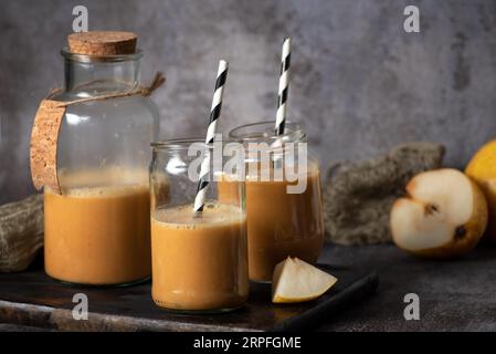 Freshly squeezed, tasty, organic, healthy pear juice, in glass jars with black and white drinking tubes, and a piece of sliced pear , on a gray backgr Stock Photo