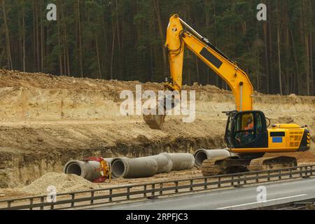 At the construction site, an escalator works along the road, pipes lie nearby. Stock Photo