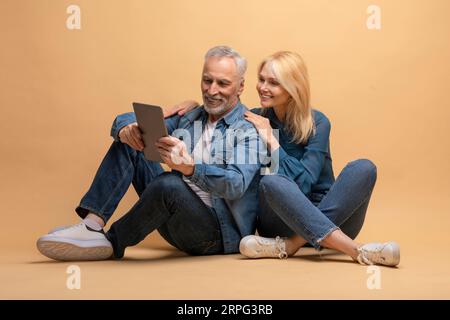 Positive senior couple using digital tablet, beige background Stock Photo